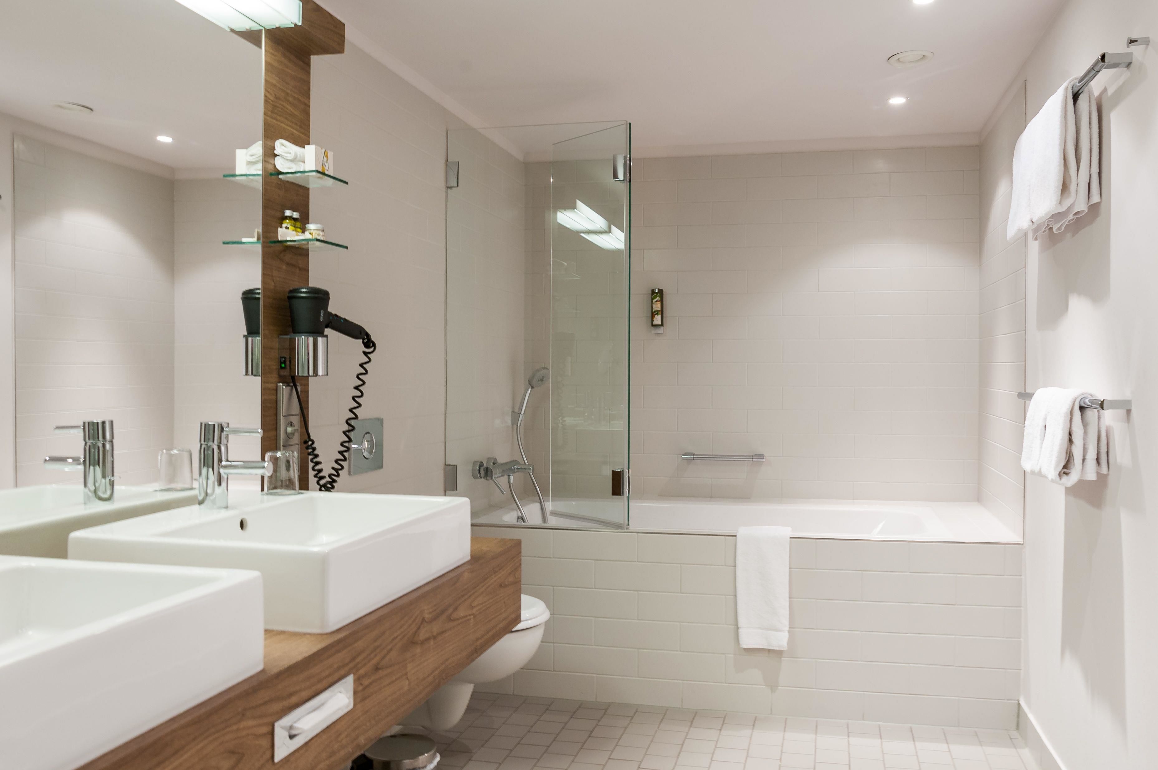 A modern bathroom with two sinks, a glass shower enclosure, a bathtub, and a wooden vanity.