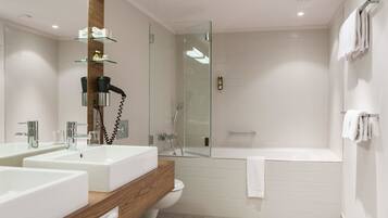 A modern bathroom with two sinks, a glass shower enclosure, a bathtub, and a wooden vanity.