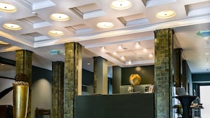 Un hall d’hôtel doté d’un plafond au design moderne, de grandes colonnes et d’un comptoir d’accueil.