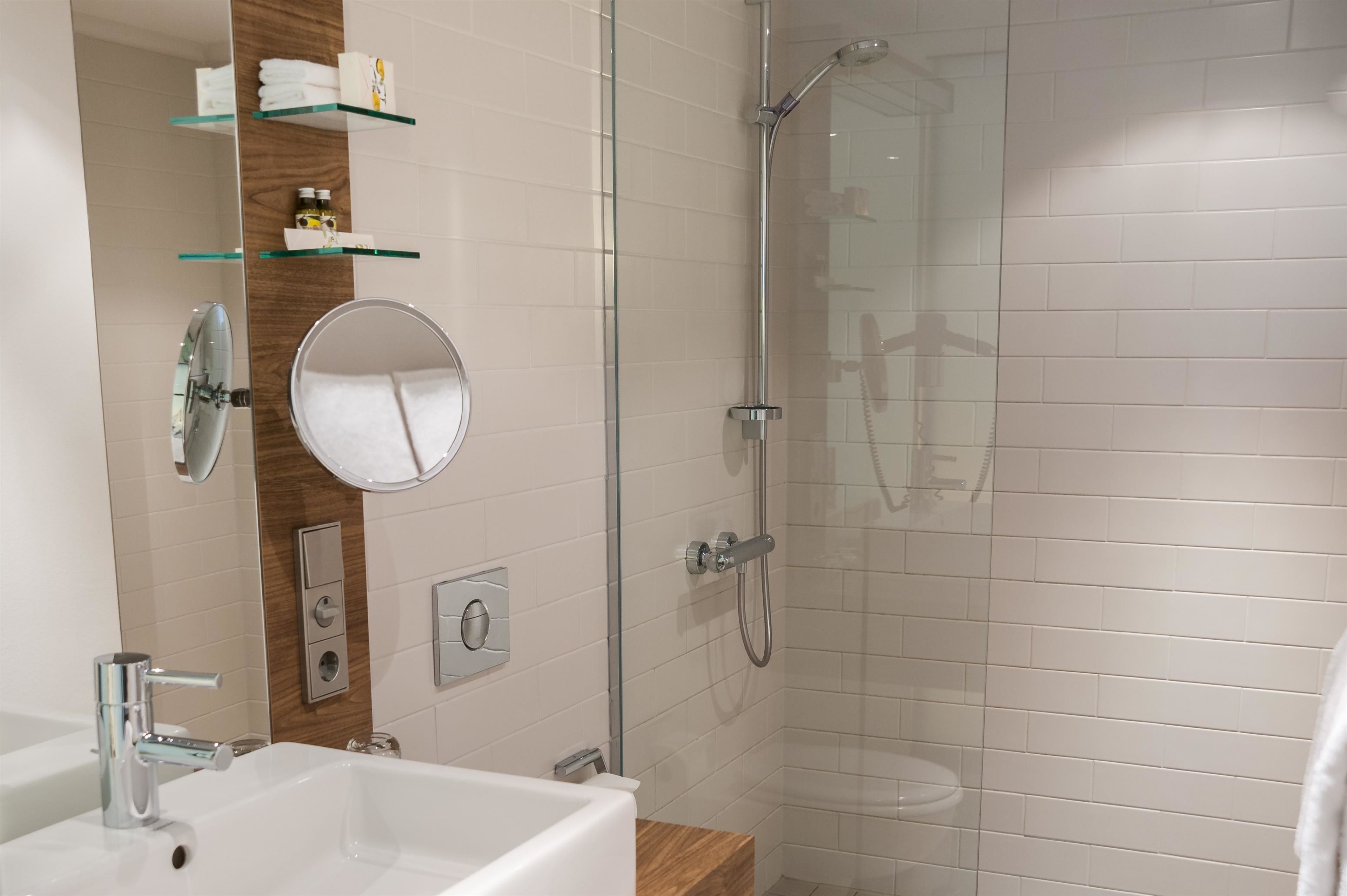 Un baño moderno con ducha envuelta en vidrio, un espejo grande y un lavabo blanco.