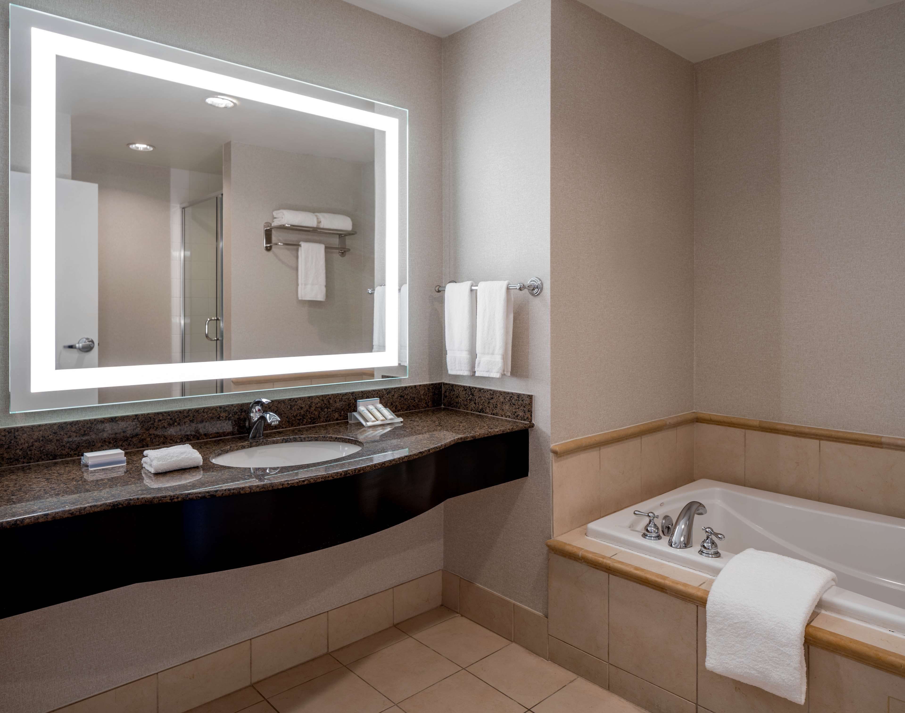 A modern bathroom with a large mirror, two sinks, a bathtub, and towels.
