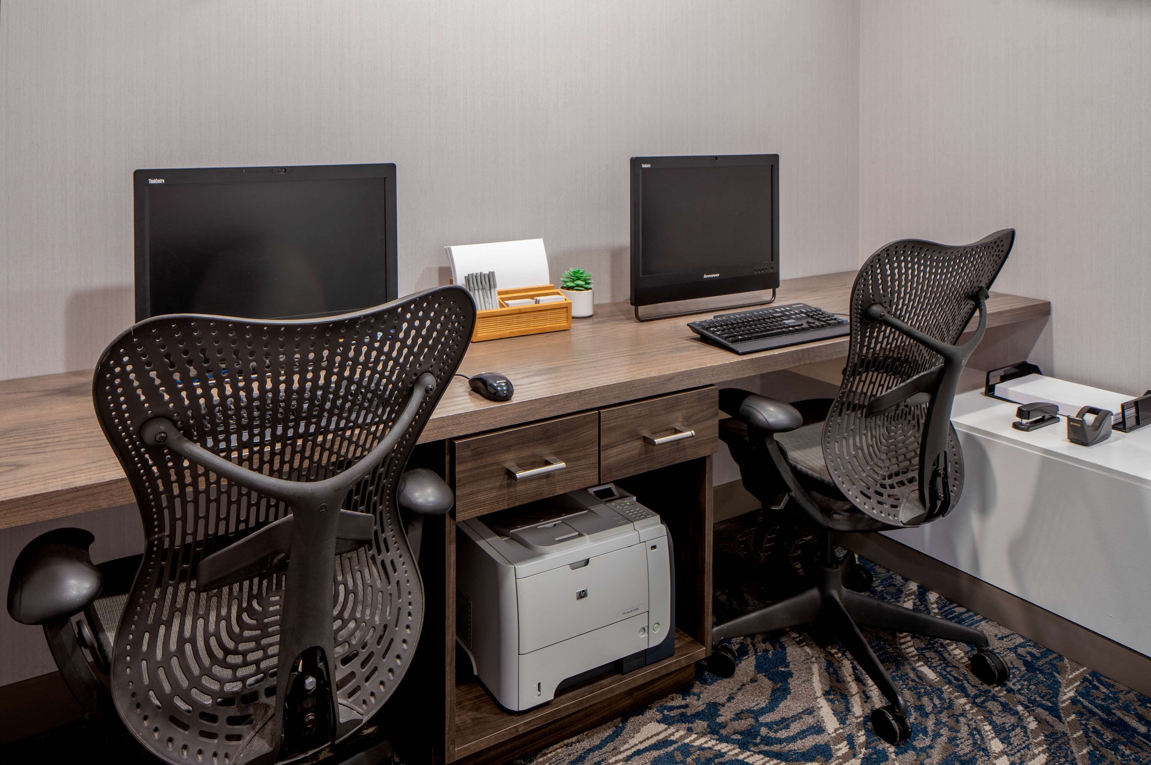 A modern office desk with two monitors, a printer, and two ergonomic chairs.