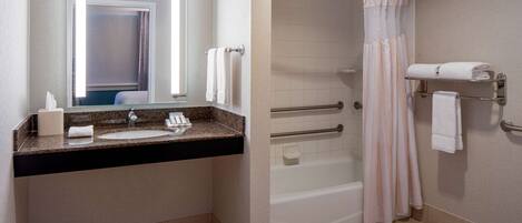 A modern bathroom with a granite countertop sink, a large mirror, a shower with a glass door, and a towel rack.