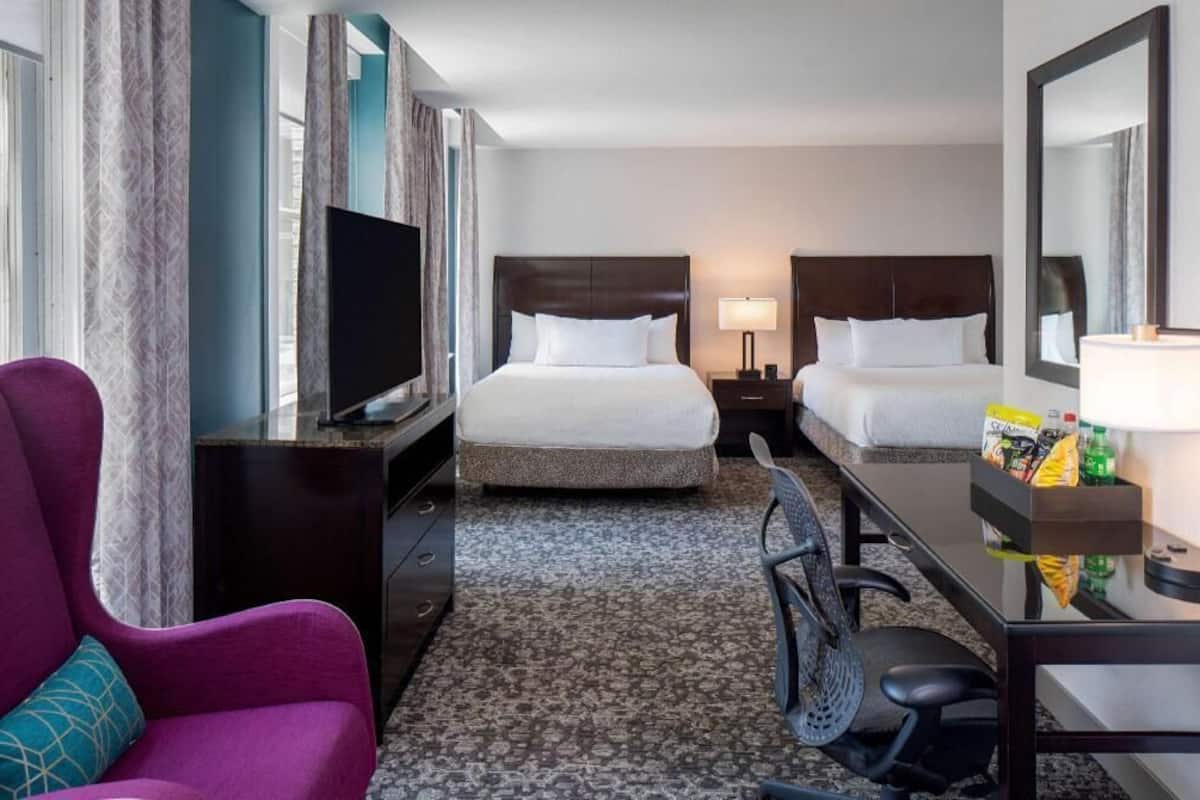 Ett hotellrum med två sängar, en TV, ett skrivbord med en stol och en minibar.