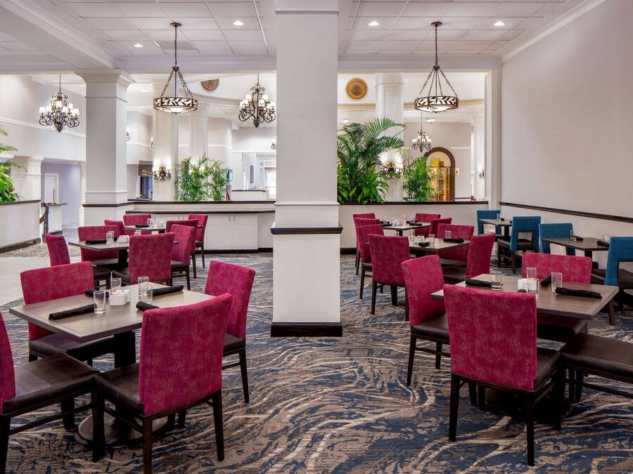 A hotel dining area with tables and chairs, chandeliers, and potted plants.
