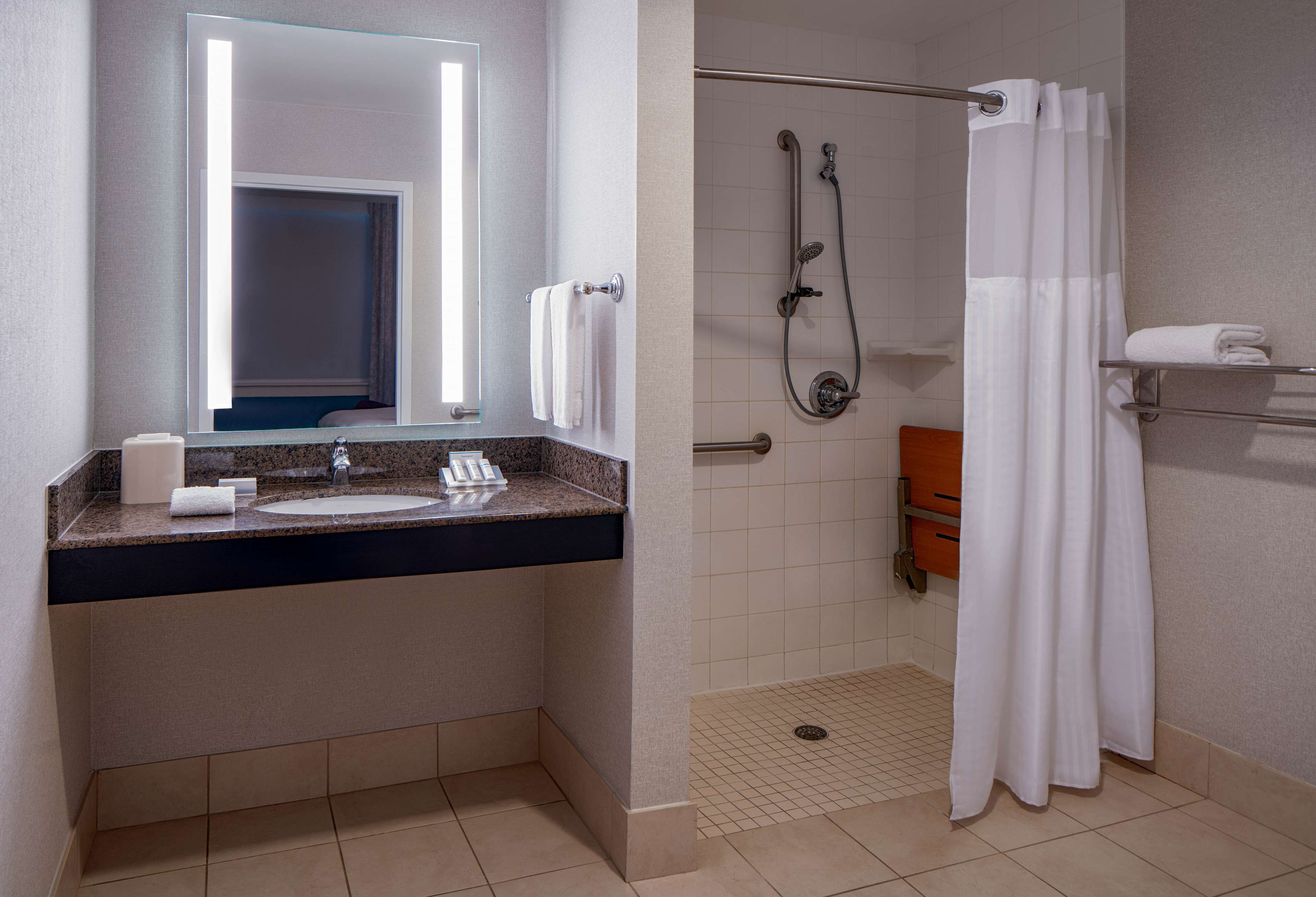 A modern bathroom with a granite countertop sink, a large mirror, a shower with a glass door, and a towel rack.