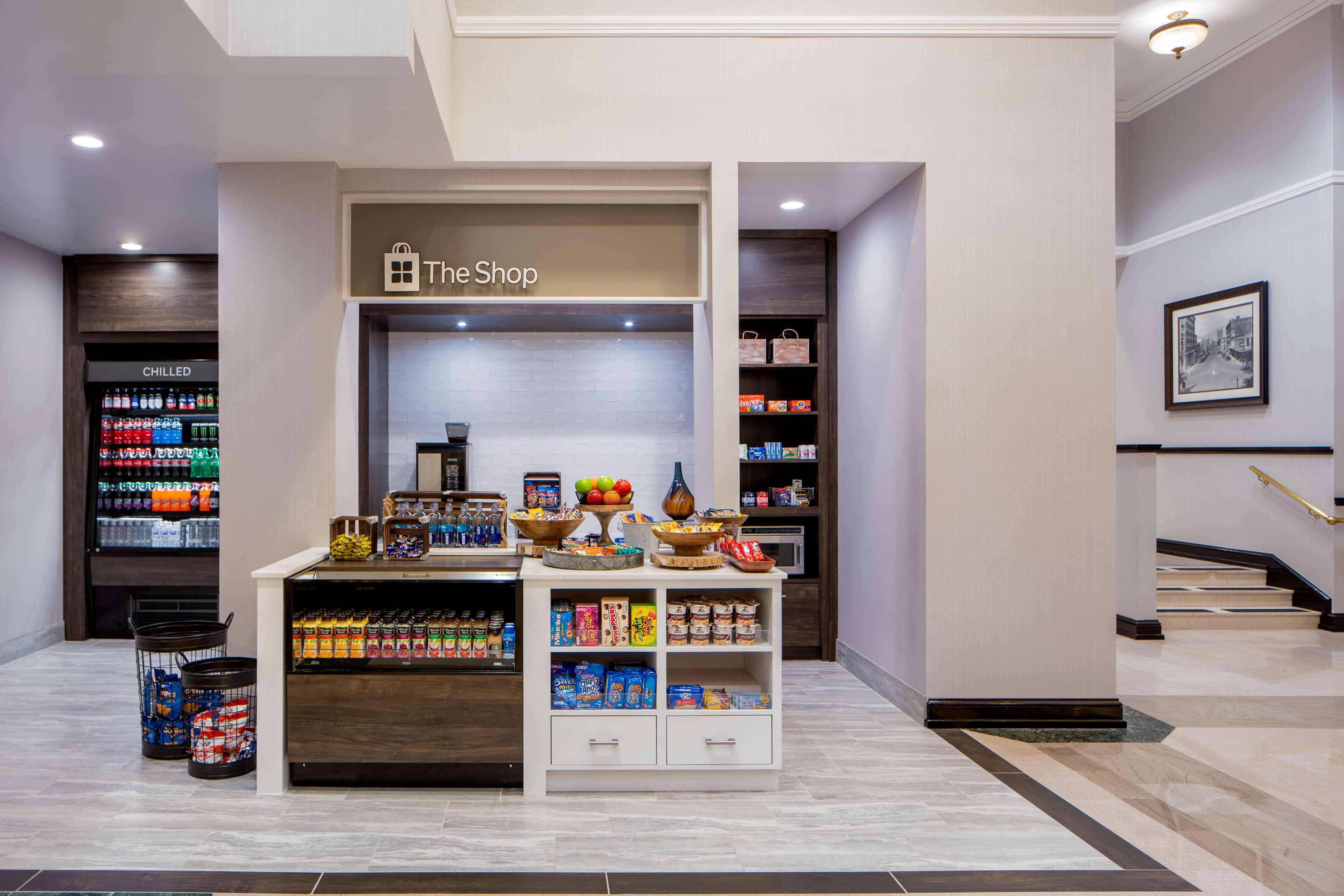 Vestíbulo de hotel con una tienda de autoservicio, una zona de bebidas refrigeradas y una escalera.