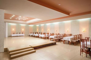 A spacious banquet hall with tiered seating, white tables, and wooden chairs. - Traian Braila (Braila)
