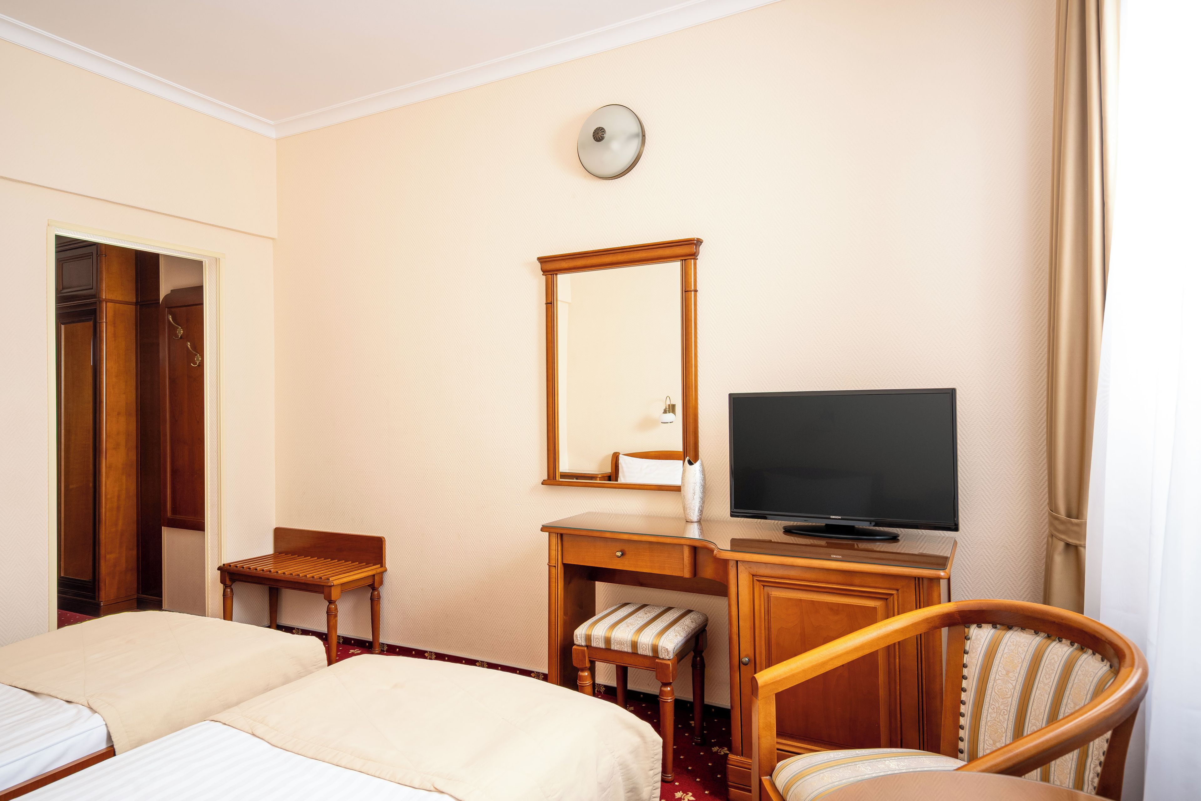 A hotel room with two beds, a desk with a television, a chair, and a mirror.