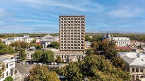 A tall building with a grid-like facade, surrounded by other buildings and trees. - Traian Braila (Braila)