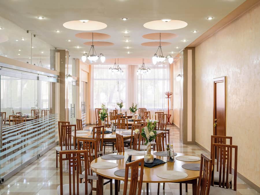 A spacious dining area with multiple tables and chairs, large windows with natural light, and a modern ceiling design.