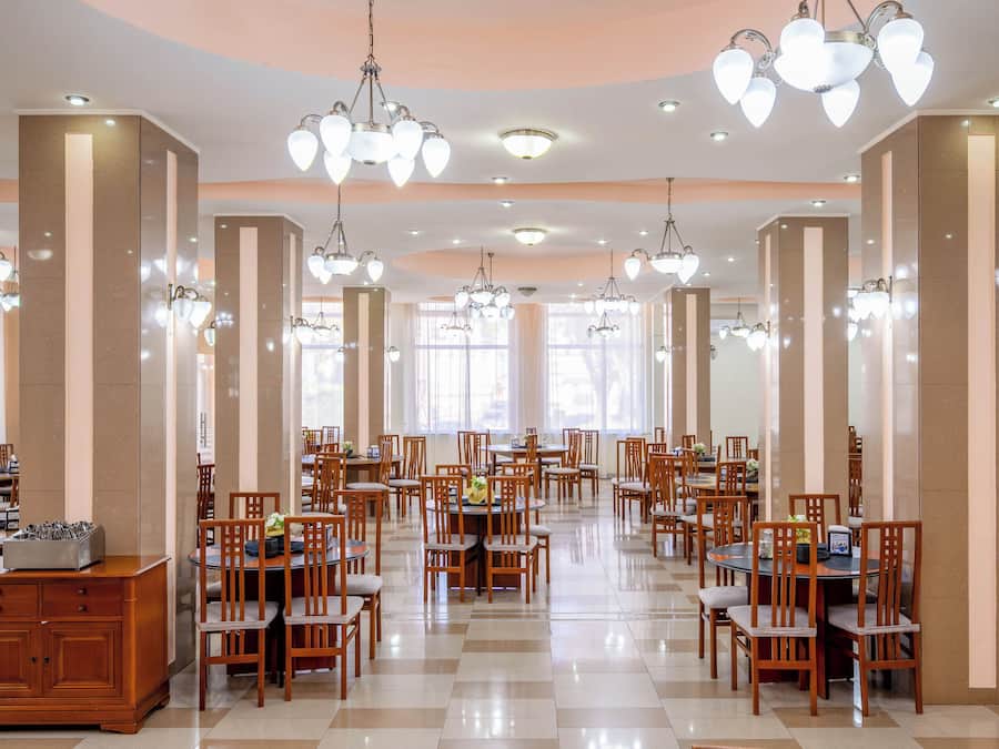 A spacious dining area with multiple tables and chairs, large windows, and decorative chandeliers.