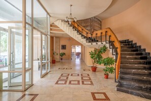 A spacious foyer with a grand staircase, potted plants, and a patterned floor. - Traian Braila (Braila)