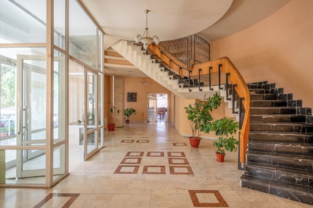 A spacious foyer with a grand staircase, potted plants, and a patterned floor.. Traian Braila