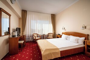 A hotel room with a bed, a desk, two chairs, a small table, and a window with curtains. - Traian Braila (Braila)