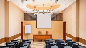 A conference room with a large screen, a podium, and rows of chairs.