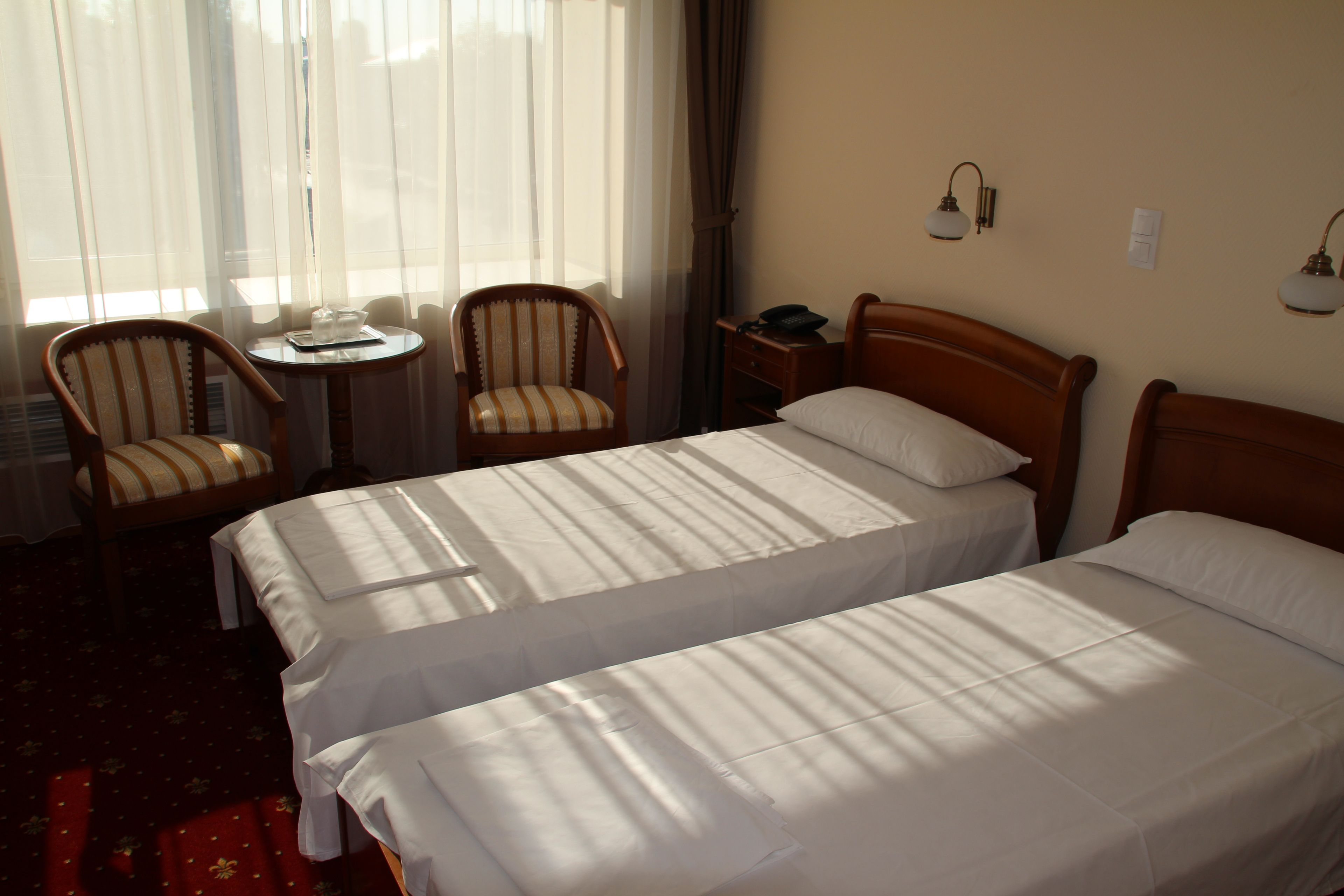 Una camera d'albergo con due letti singoli, un piccolo tavolo con sedie, un comodino e una finestra con tende.