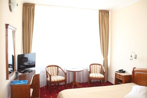 A hotel room with a bed, a desk with a television, two chairs, a small table, and a window with curtains. - Traian Braila (Braila)