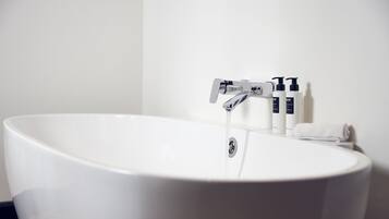 Un baño moderno con una bañera independiente, un grifo y artículos de aseo a un lado.
