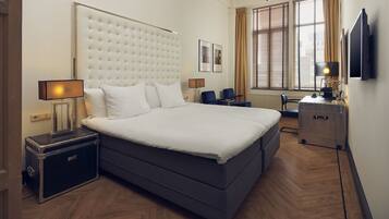 A modern hotel room with a large bed, bedside tables, a desk, and a TV.