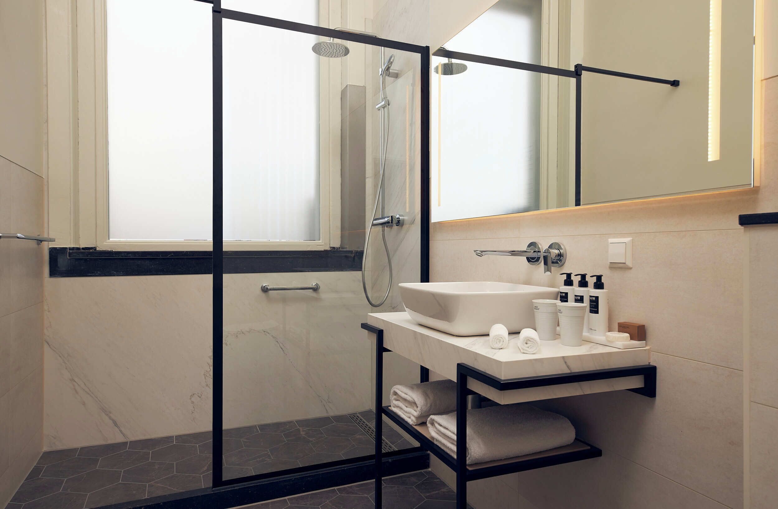 Un baño moderno con ducha de vidrio, un lavabo blanco con encimera de mármol y un espejo sobre el lavabo.