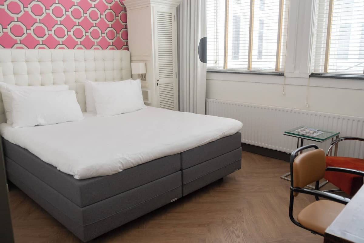 A neatly made bed with white bedding, a grey headboard, and a patterned wall behind it.