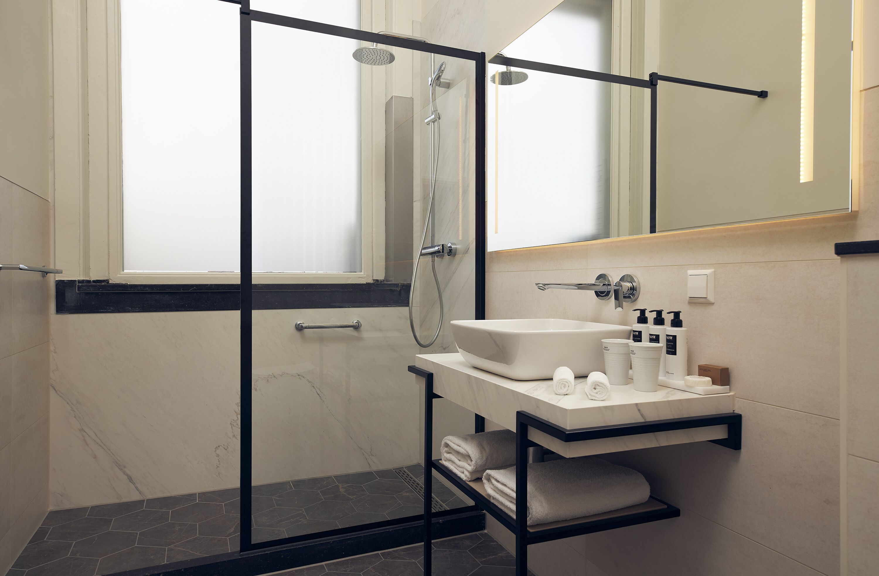 Un baño moderno con ducha envuelta en vidrio, lavamanos de mármol y un perchero para toallas.