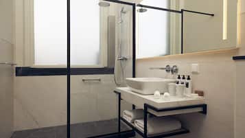 Un baño moderno con ducha envuelta en vidrio, lavamanos de mármol y un perchero para toallas.