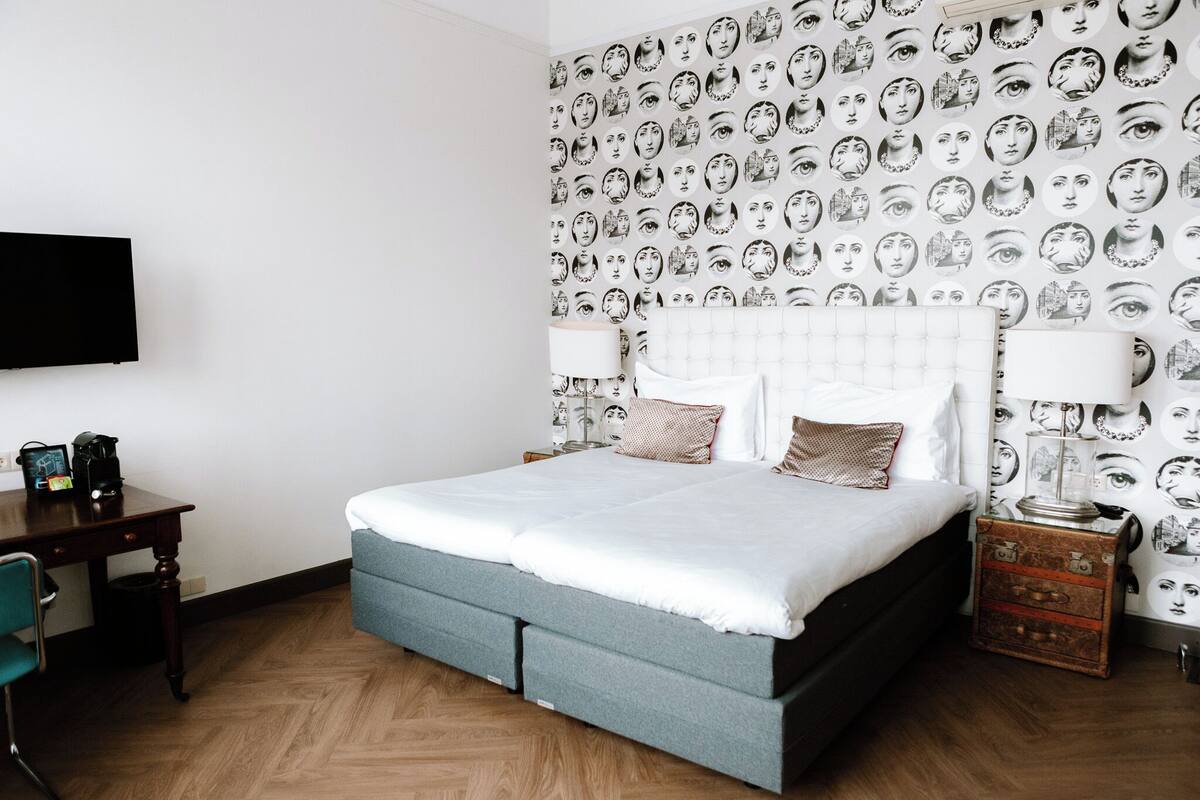 A bedroom with a bed, a desk, a chair, a lamp, and a wall with a face pattern.