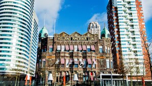 Un edificio histórico con un letrero que dice "HOLLAND AMERICA LJN", rodeado de modernos rascacielos.