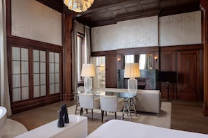 A spacious room with a glass dining table, white upholstered chairs, and a fireplace. - Hotel New York (Rotterdam)