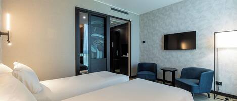 Una habitación de hotel con dos camas, televisión, dos sillones y una mesita.