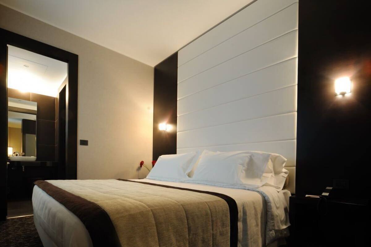 Een hotelkamer met een groot bed, een nachtkastje, een spiegel en een wandlamp.
