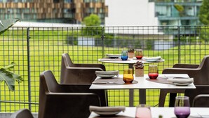 A dining area with tables and chairs, a view of buildings, and a fenced outdoor space.