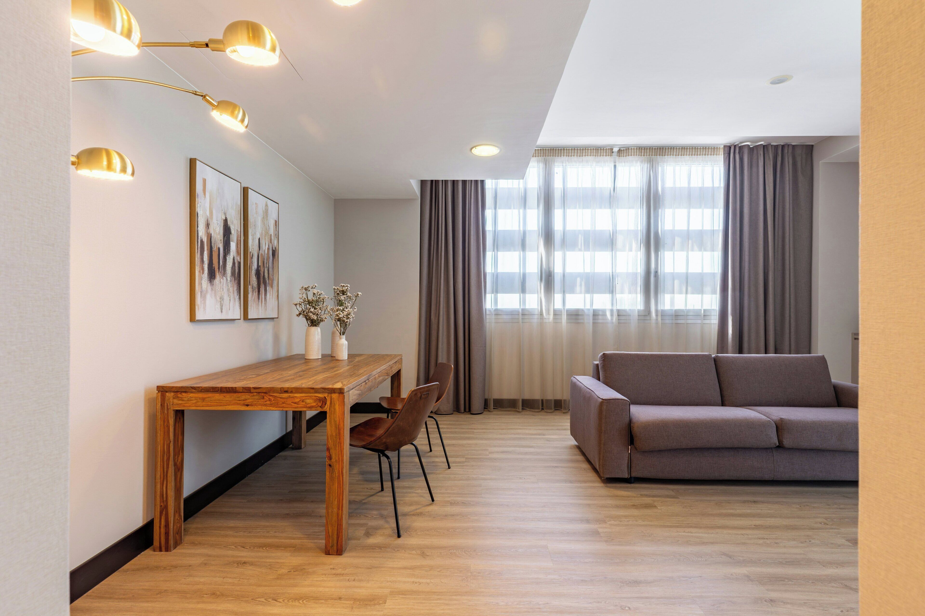 Een moderne woonkamer met een bank, een houten eettafel met stoelen, en een groot raam met gordijnen.
