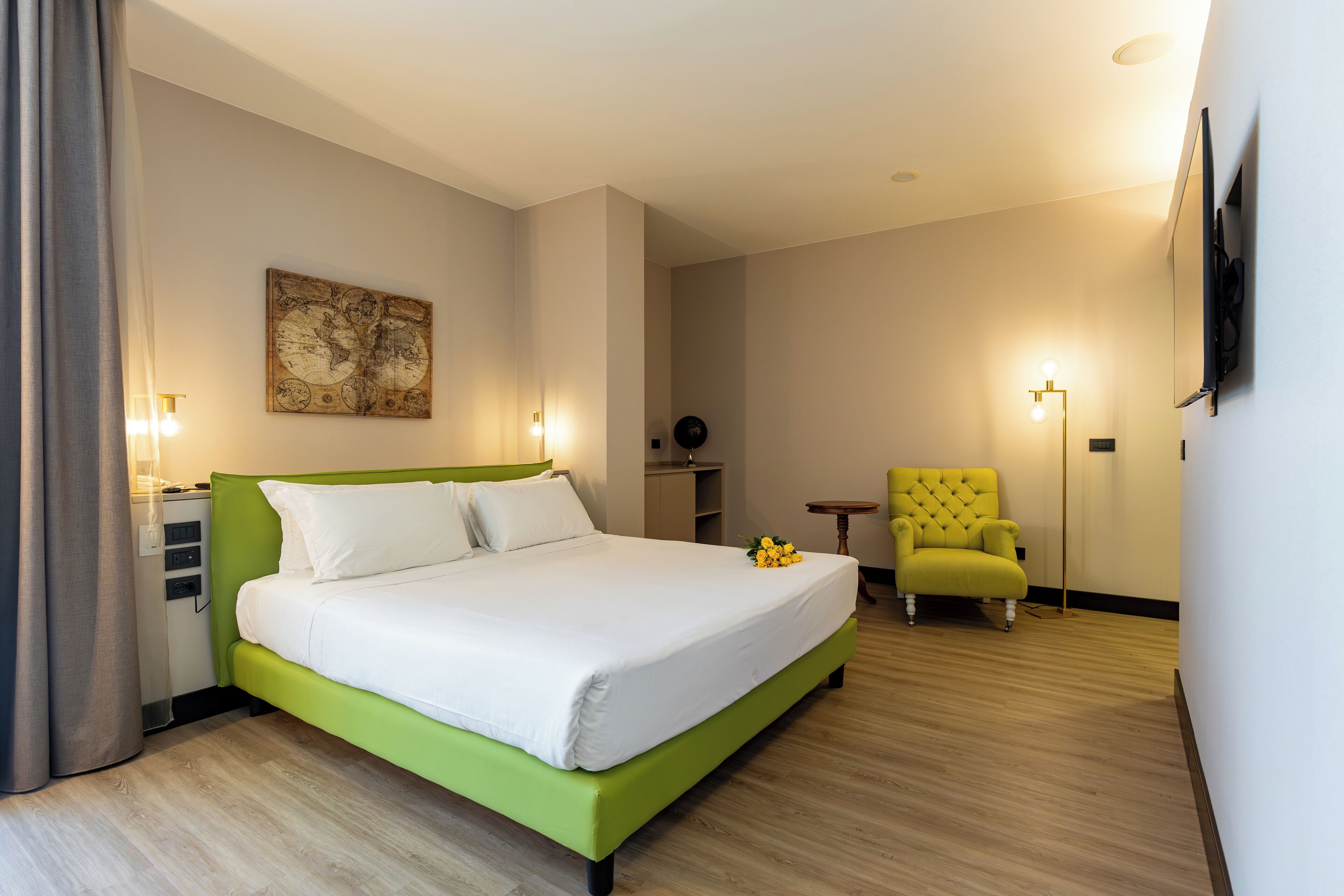 Camera d'albergo con un letto verde, una TV a schermo piatto montata a parete, un piccolo tavolo e una poltrona gialla.