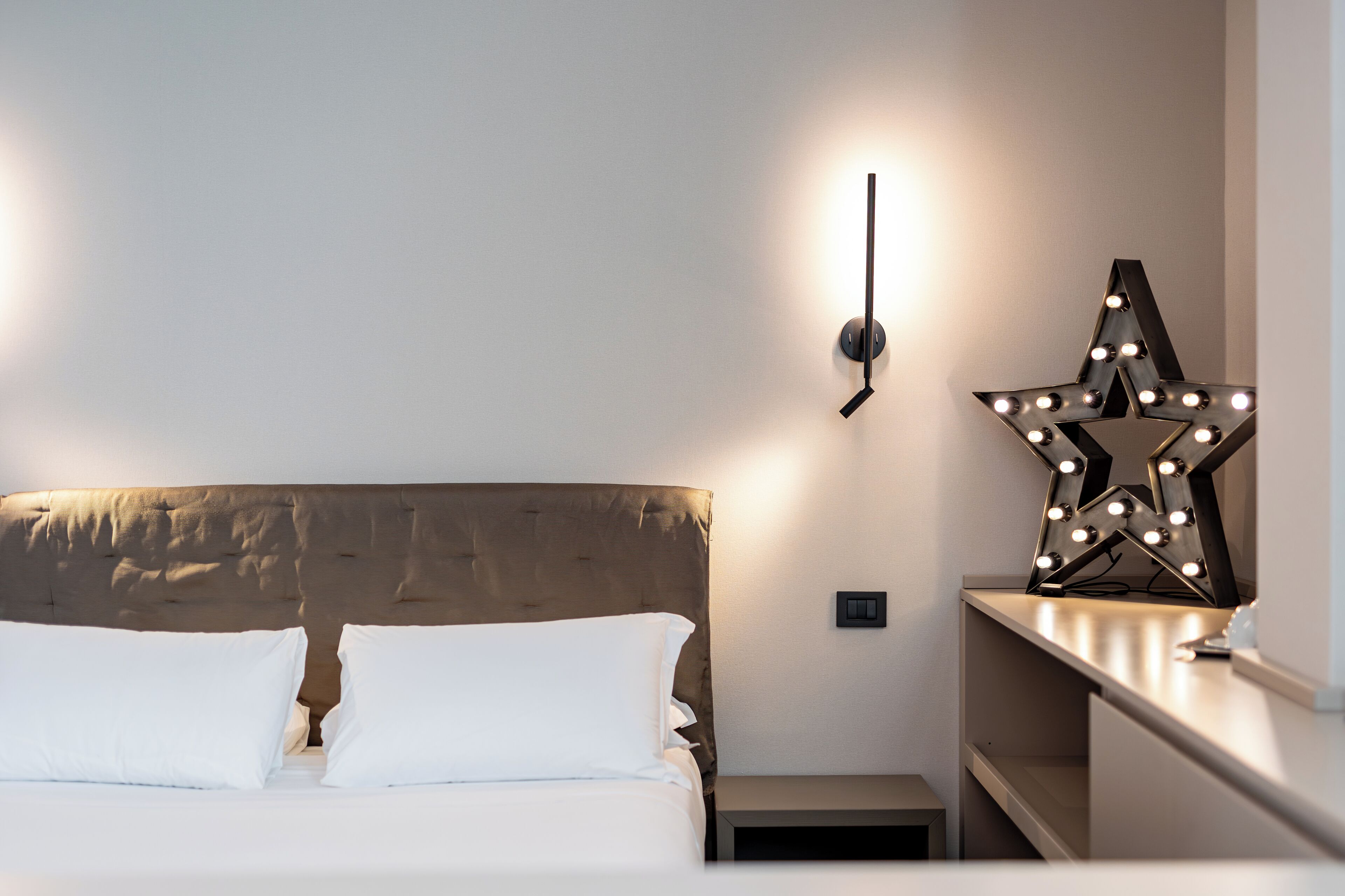 A neatly made bed with white pillows and a headboard, a bedside table with a lamp, and a wall-mounted star-shaped light fixture.
