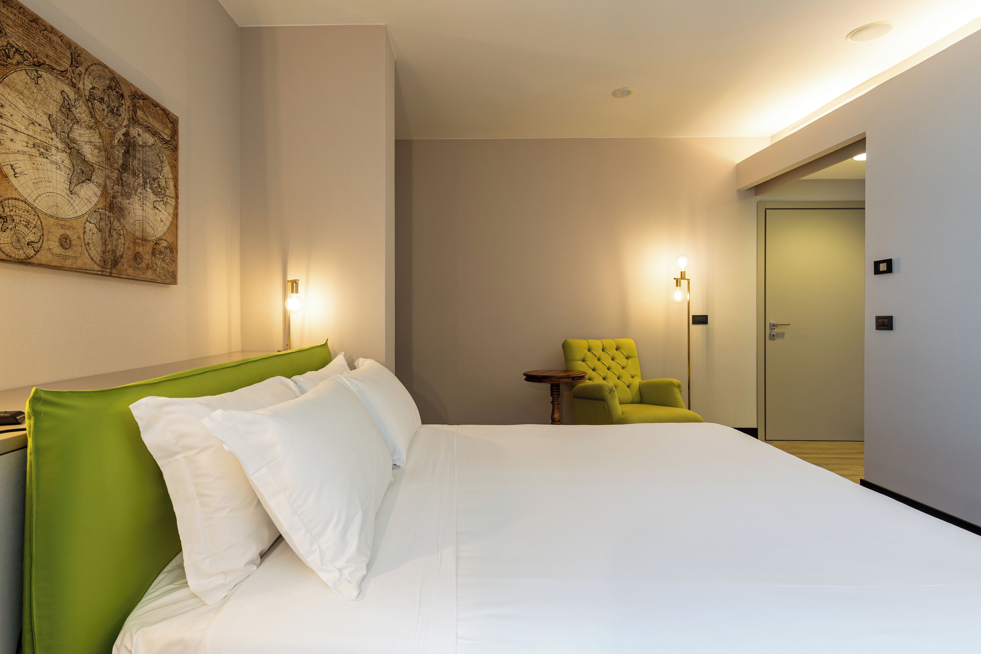 A hotel room with a large bed, a green headboard, a map on the wall, and a yellow armchair.