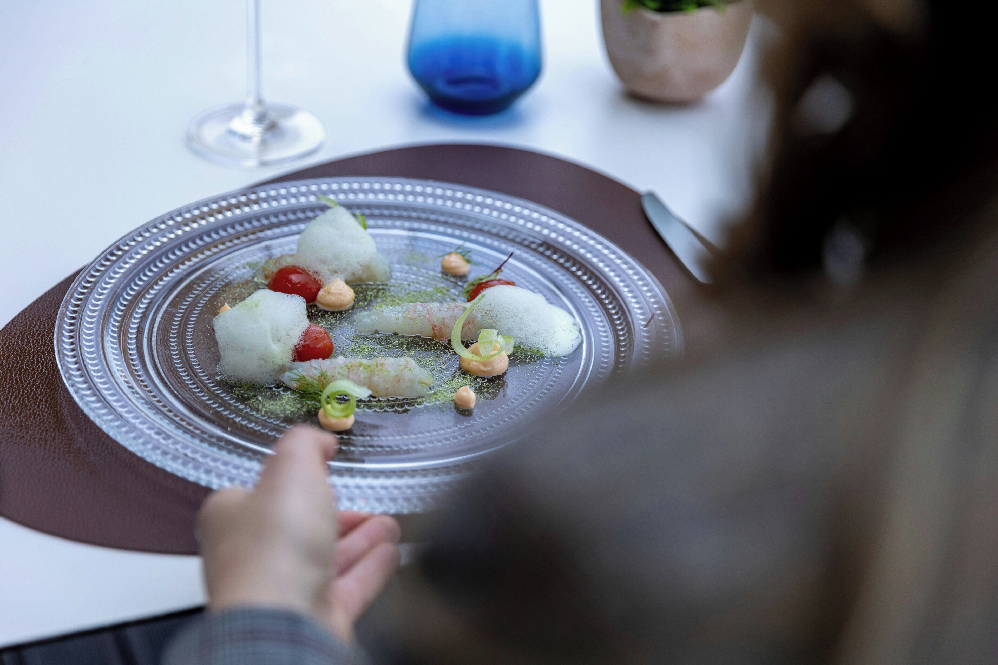 Une table à manger avec une assiette de nourriture, un verre d’eau et un vase bleu.