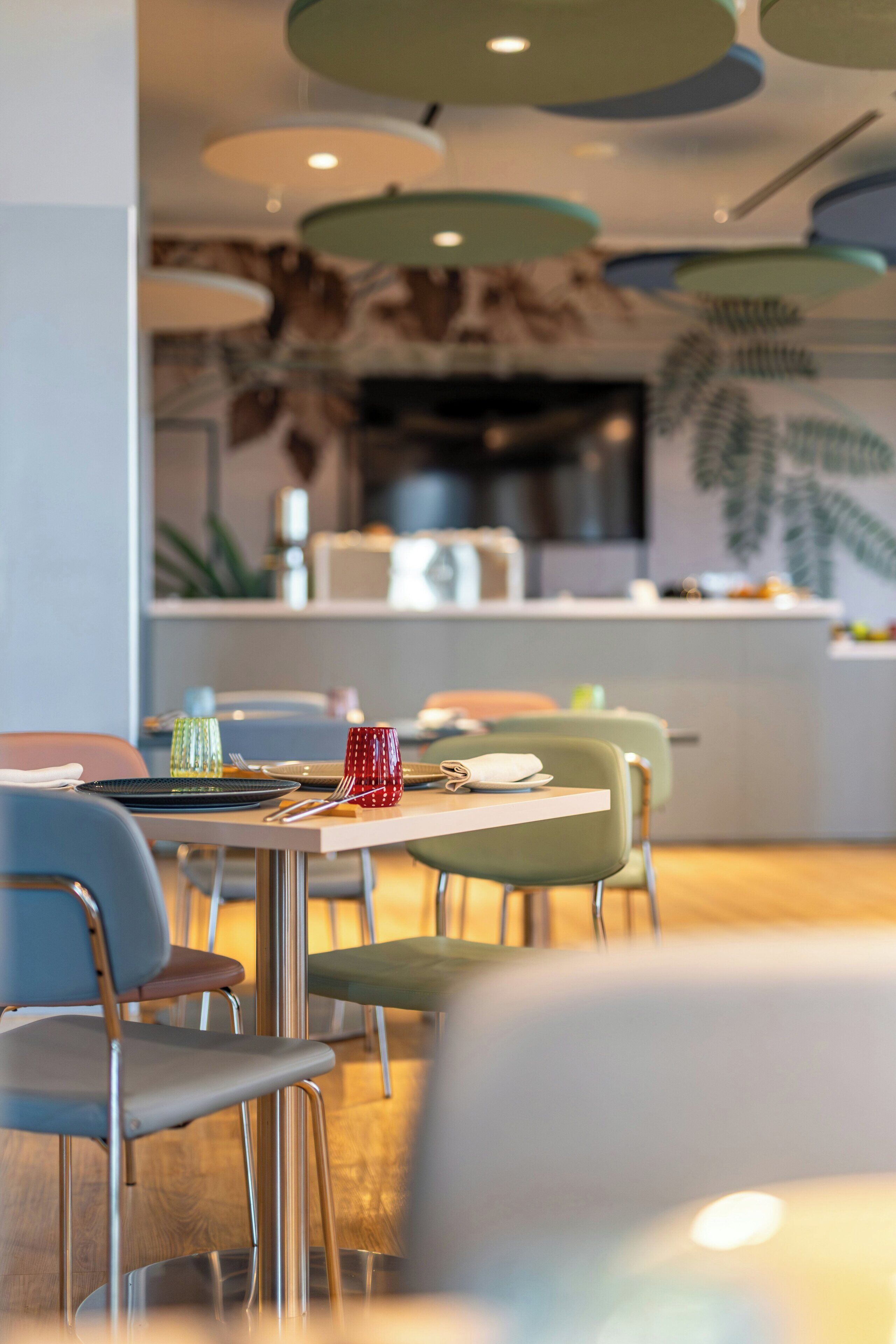 A modern dining area with tables and chairs, a kitchen in the background, and a ceiling with circular light fixtures.