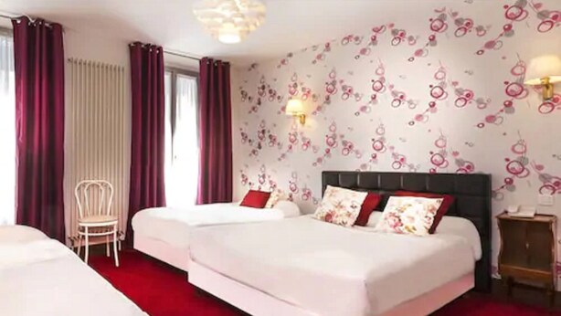 A hotel room with two beds, a red carpet, a chair, and a wall with floral wallpaper.