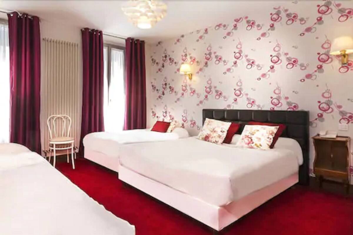 A hotel room with two beds, a red carpet, a chair, and a wall with floral wallpaper.