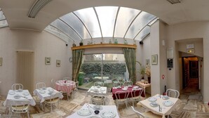 A dining area with multiple tables set for meals, a large skylight, and a view of the garden.