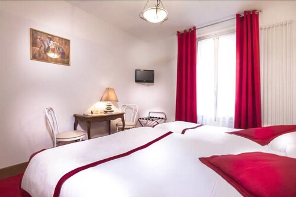 A hotel room with a bed, a desk with a lamp, a television, and a painting on the wall.