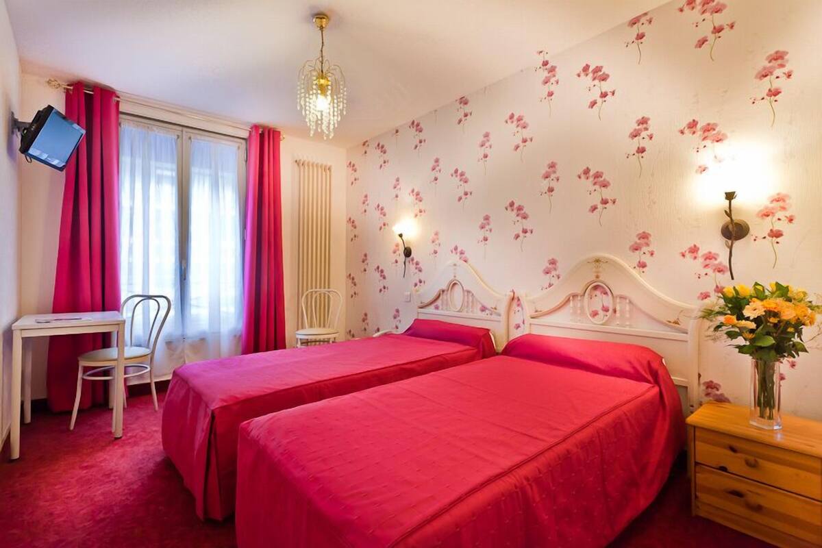 A hotel room with two beds, a desk, a chair, a TV, and a decorative wall.