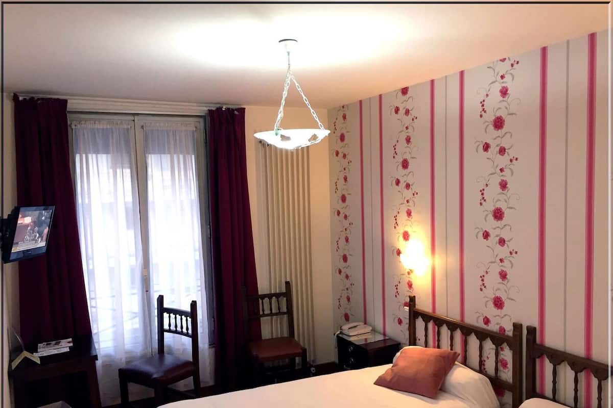 A hotel room with a bed, a desk with a chair, a small table with a telephone, and a wall-mounted TV.