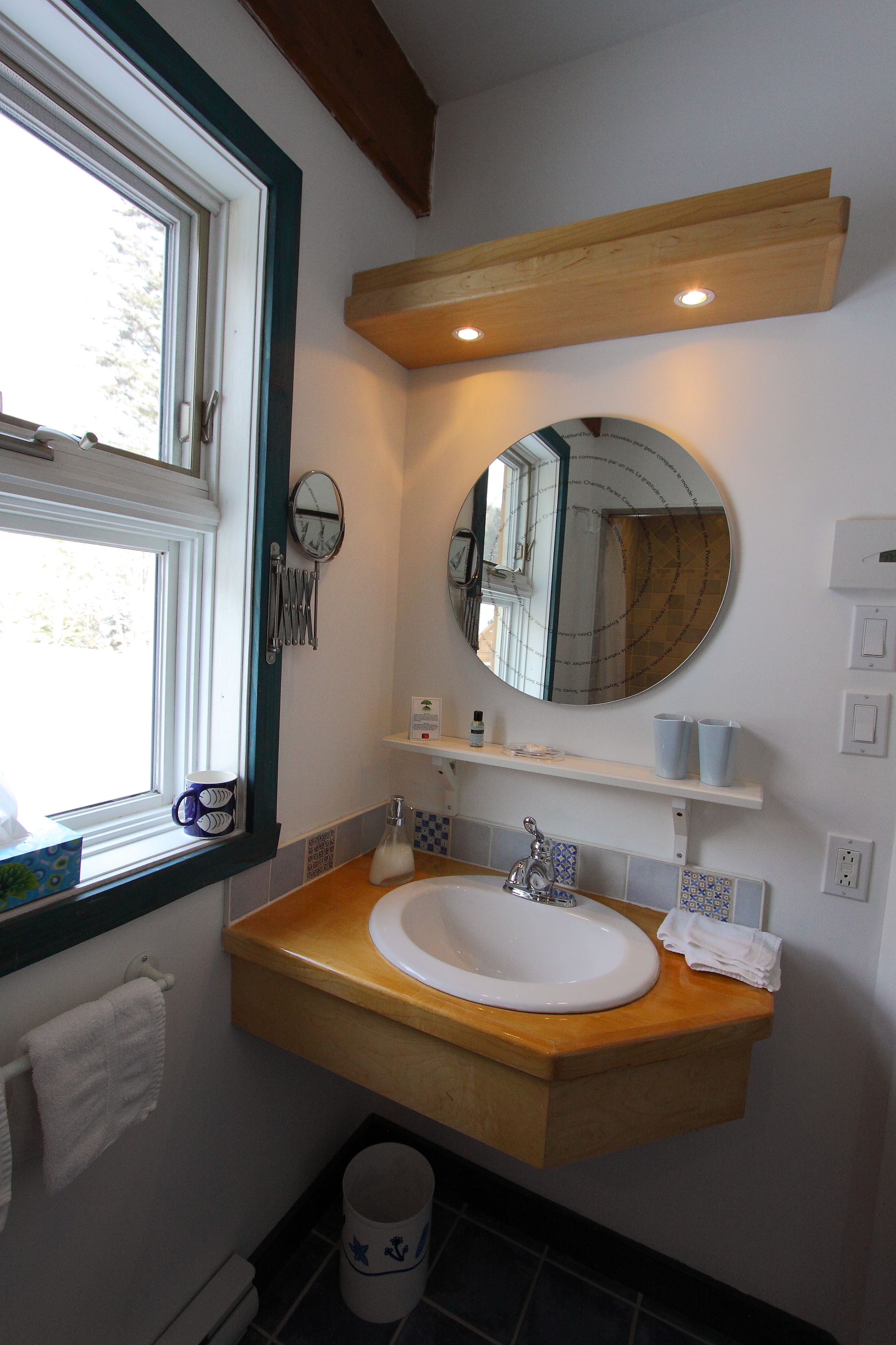 A bathroom with a wooden vanity, a round mirror, a window, and a towel rack.