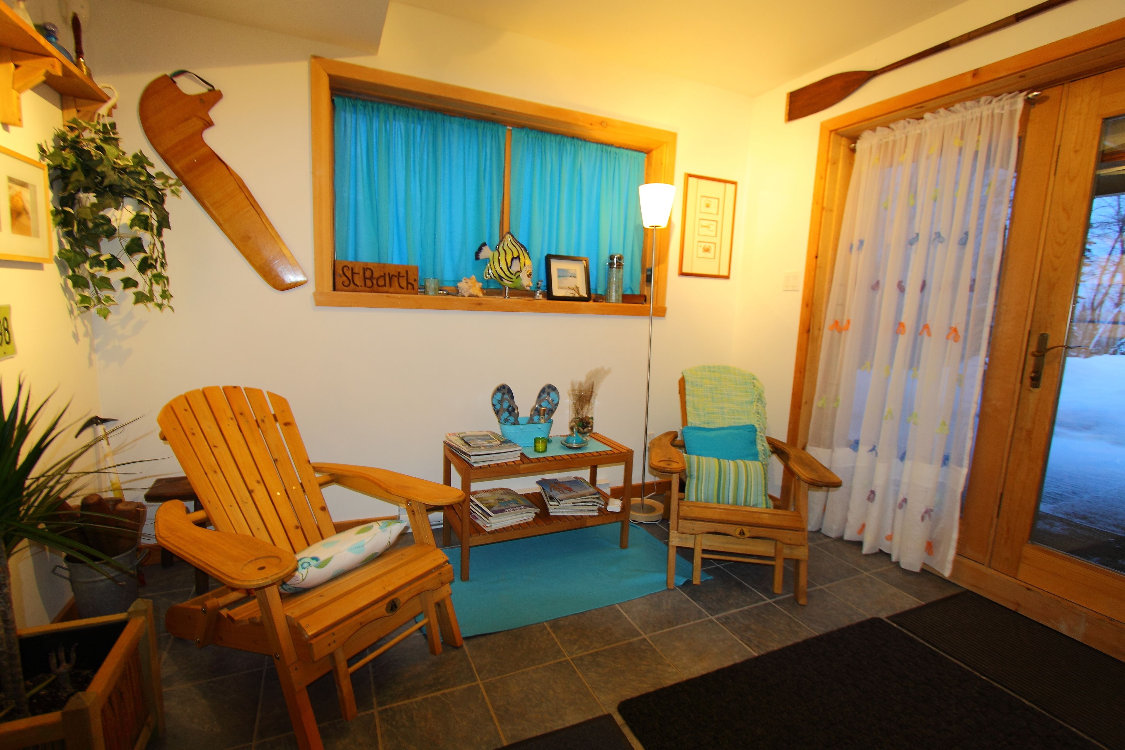A cozy living room with wooden furniture, a window with blue curtains, and a view of the outside.