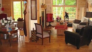 A wooden cabin interior with a dining table, chairs, a sofa, and a large window. - Escale du Nord (Mont-Tremblant)