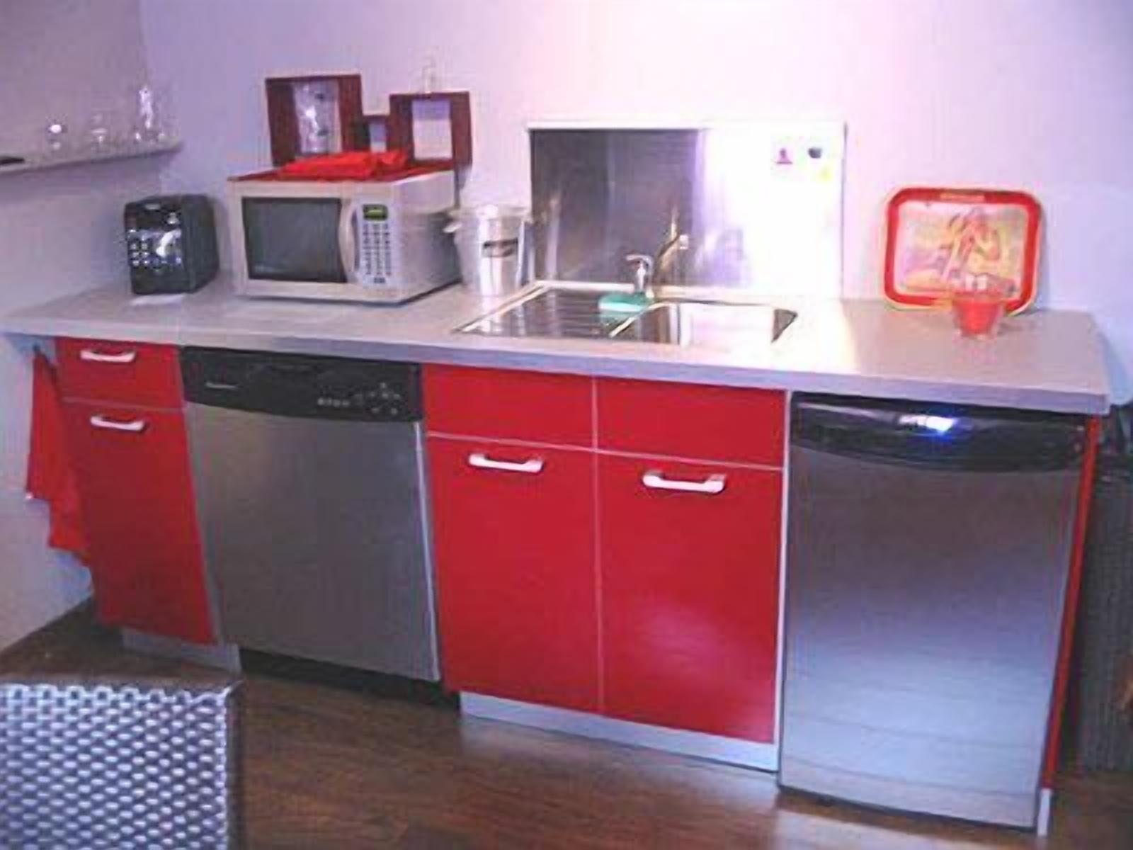 A compact kitchen with a microwave, coffee maker, and a red toaster on the countertop.